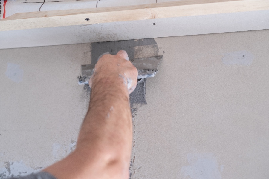 Un chantier de rénovation où un artisan fixe une bavette métallique au pied d’un mur pour assurer l’étanchéité du raccord toiture-mur