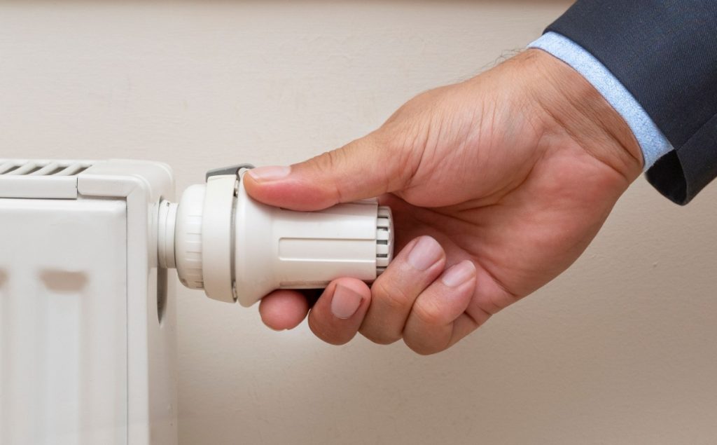 Un radiateur en fonte partiellement ouvert, tandis qu’une main coupe l’arrivée d’eau avant le remplacement du robinet