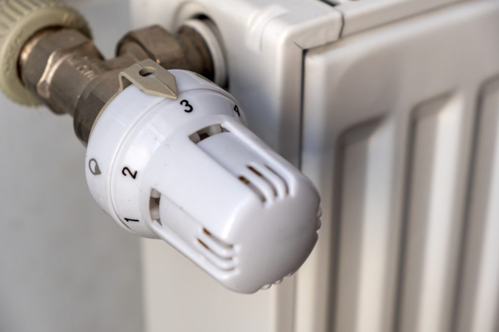 Un technicien retire l’ancien robinet d’un radiateur relié au chauffage collectif, avec les outils posés au sol