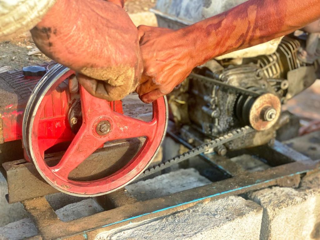 Main d'un homme qui change la courroie d'une motobineuse