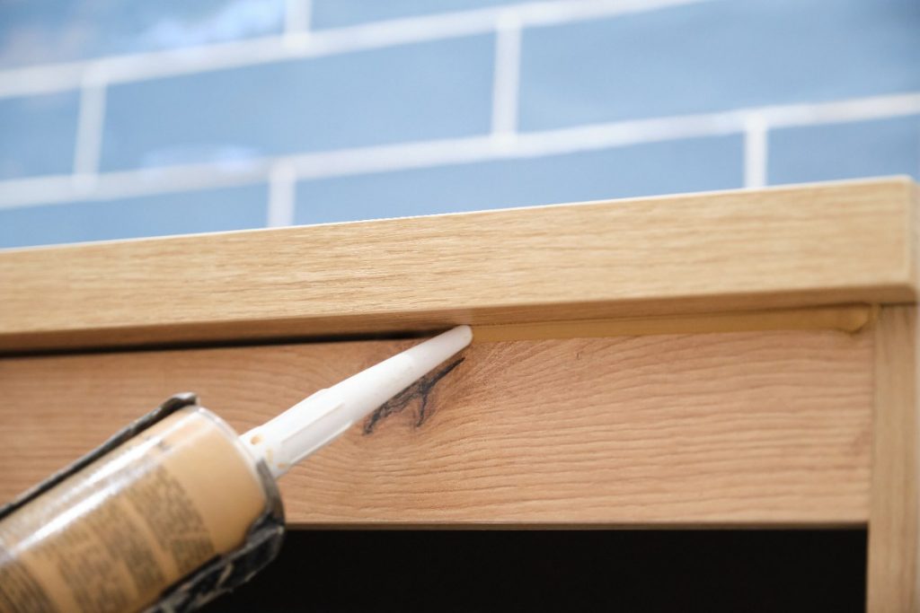 Une personne qui applique du calfeutrage sur du bois