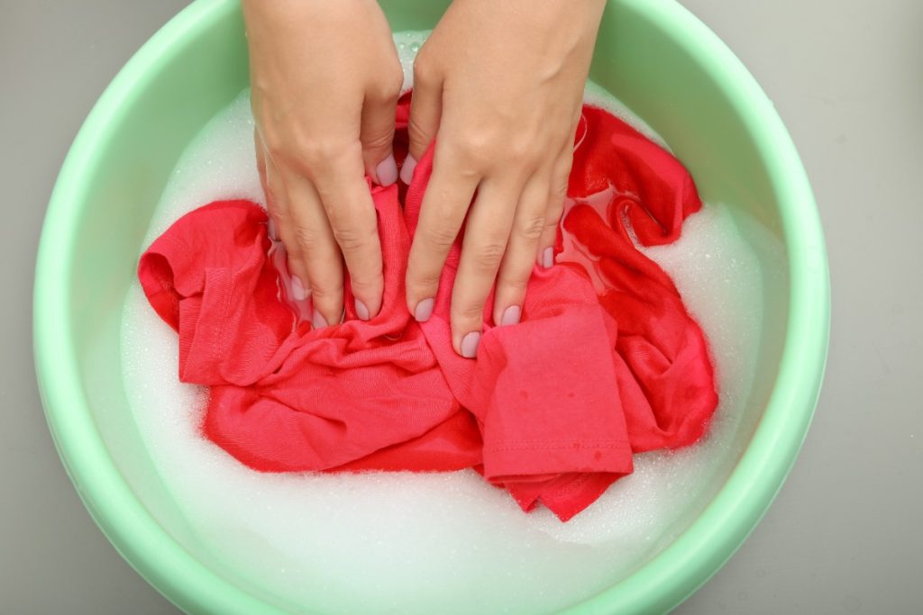 Une personne qui lave un linge rouge dans une cuvette