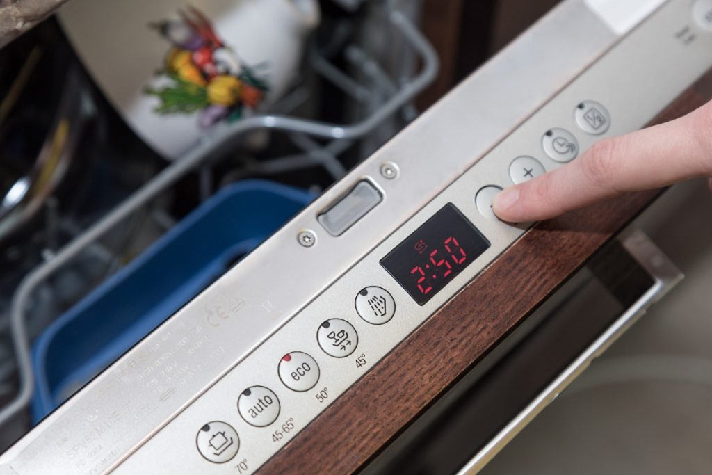 Un doigt qui appuie sur le bouton de la lave-vaisselle