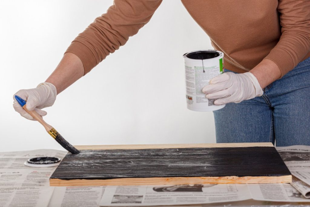 Peut-on utiliser de l'huile de vidange pour protéger le bois extérieur ? Une femme peignant une planche en bois avec de l'huile de vidange