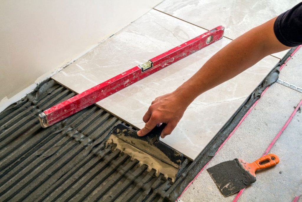 Quelle surface un carreleur professionnel peut-il couvrir en une journée de travail ? Un homme posant du carrelage en utilisant du niveau et de la truelle