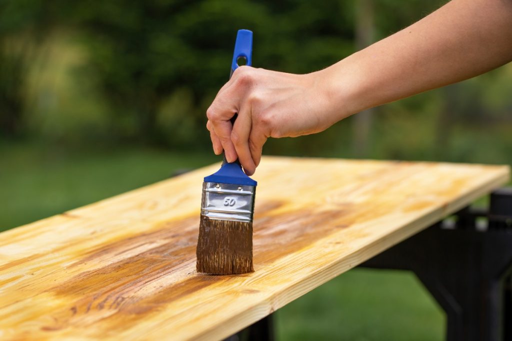 Peut-on utiliser de l'huile de vidange pour protéger le bois extérieur ? Main tenant un pinceau et peint du bois avec de l'huile de vidange