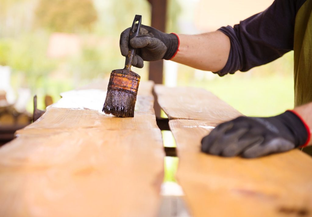 Peut-on utiliser de l'huile de vidange pour protéger le bois extérieur ? Une personne peignant du bois extérieur avec de l'huile de vidange