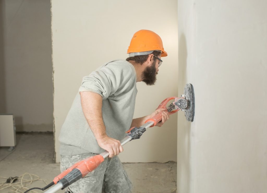 Un homme barbu ponçant le mur