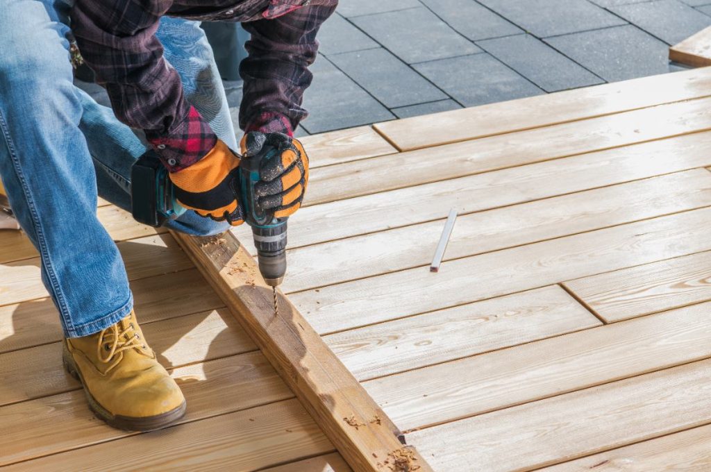 Un homme qui perce une planche en bois pour une installation de terrasse