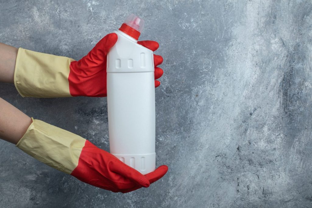 Mains gantées tenant des produits nettoyant ménager