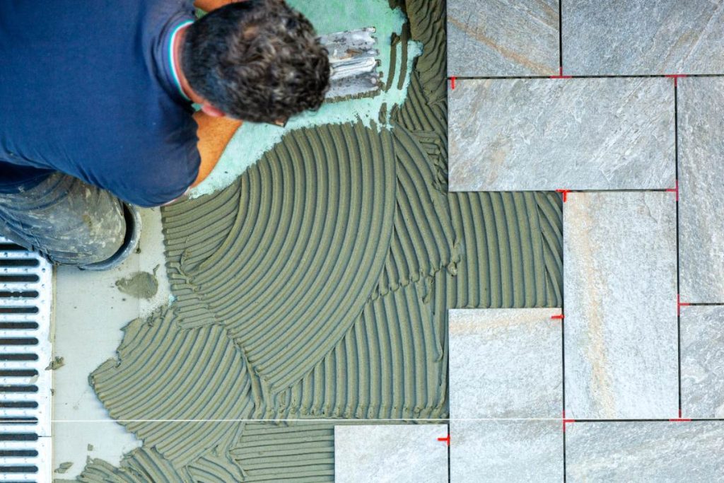 Un ouvrier posant du carrelage au sol et appliquant du mortier