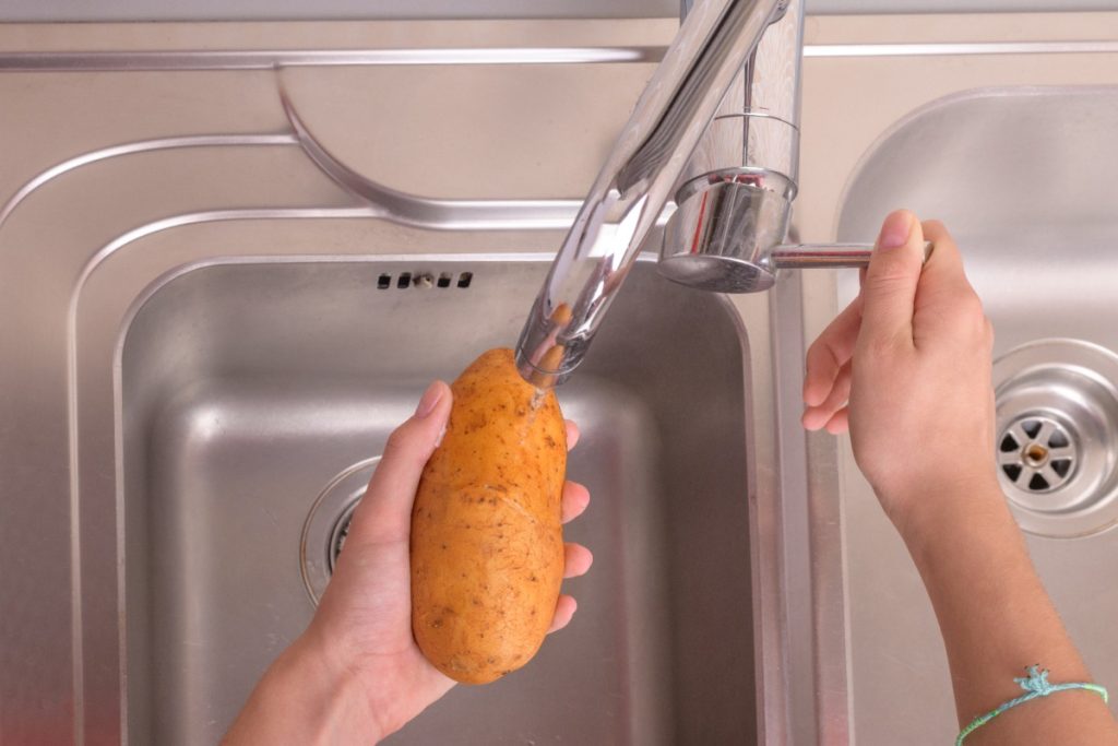 Une personne qui lave une pomme de terre dans un évier