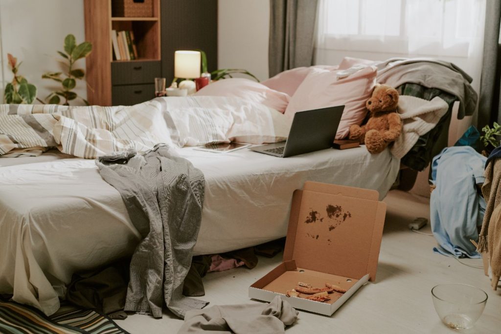 Une chambre en désordre avec un ordinateur portable sur le lit