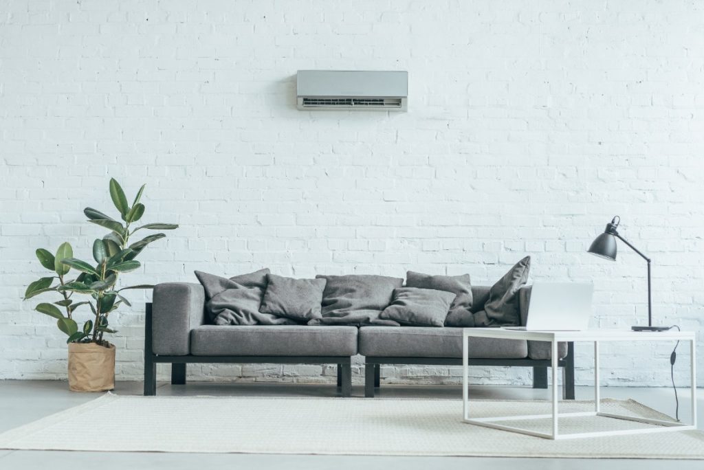 Un climatiseur installé au-dessus d'un canapé gris avec des coussins
